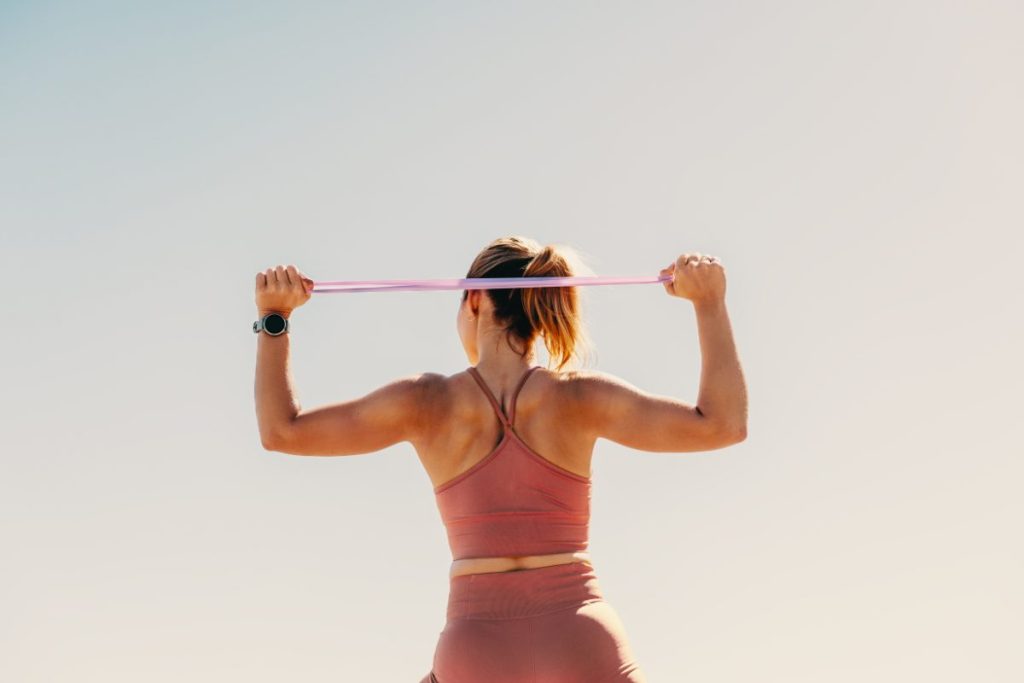 A person in athletic wear stretching with a resistance band overhead, seen from behind