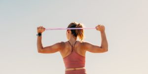 A person in athletic wear stretching with a resistance band overhead, seen from behind