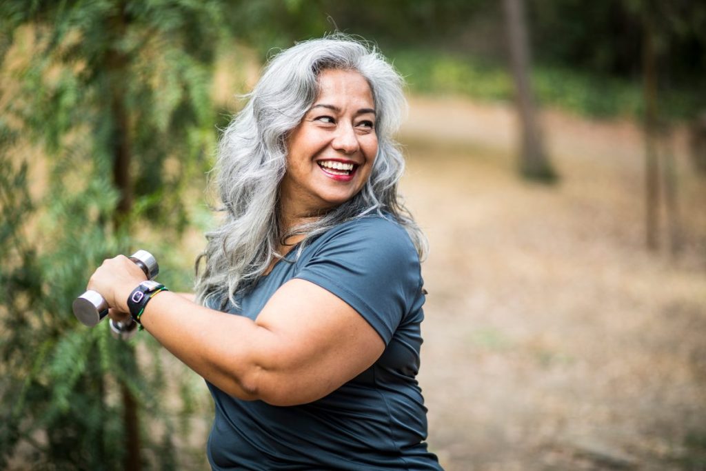 A smiling woman flexing her bicep outdoors on a trail