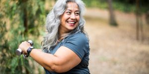 A smiling woman flexing her bicep outdoors on a trail